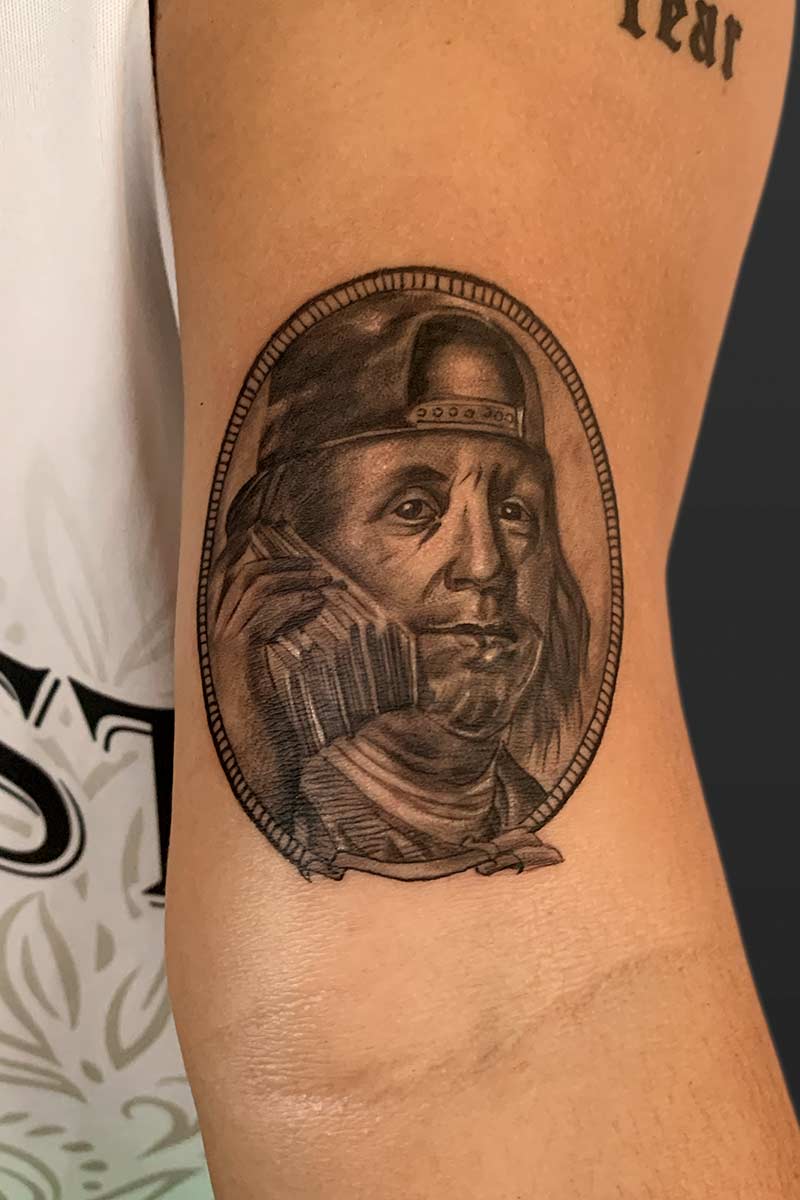 Legacy Tattoo| Micro-realism tattoo of Benjamin Franklin, wearing a cap backwards and holding a stack of money