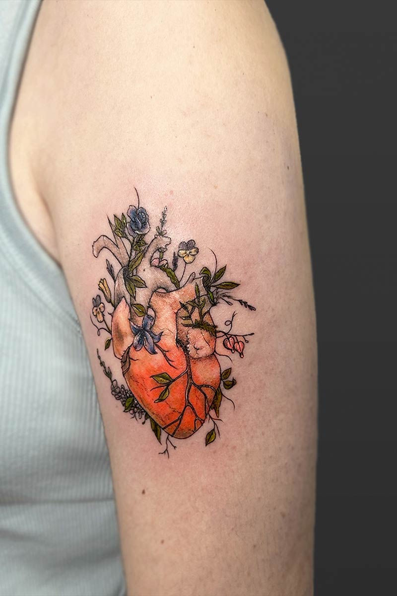 Legacy Tattoo| Fineline, coloured tattoo of an orange human heart, different coloured flowers and foliage