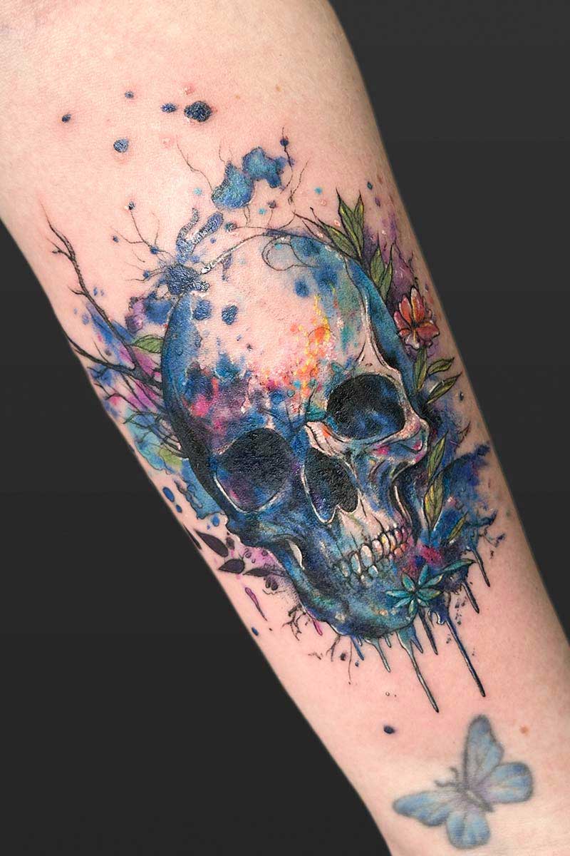 Legacy Tattoo| Watercolour tattoo of a human skull and flowers with splashes and drips of ink