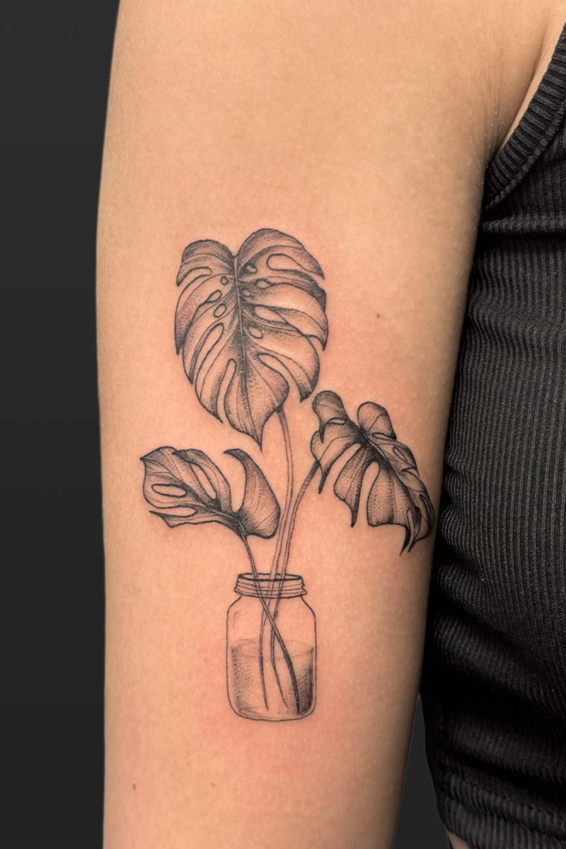 Legacy Tattoo| Black and grey, realism tattoo of a monsterra plant in a jar of water