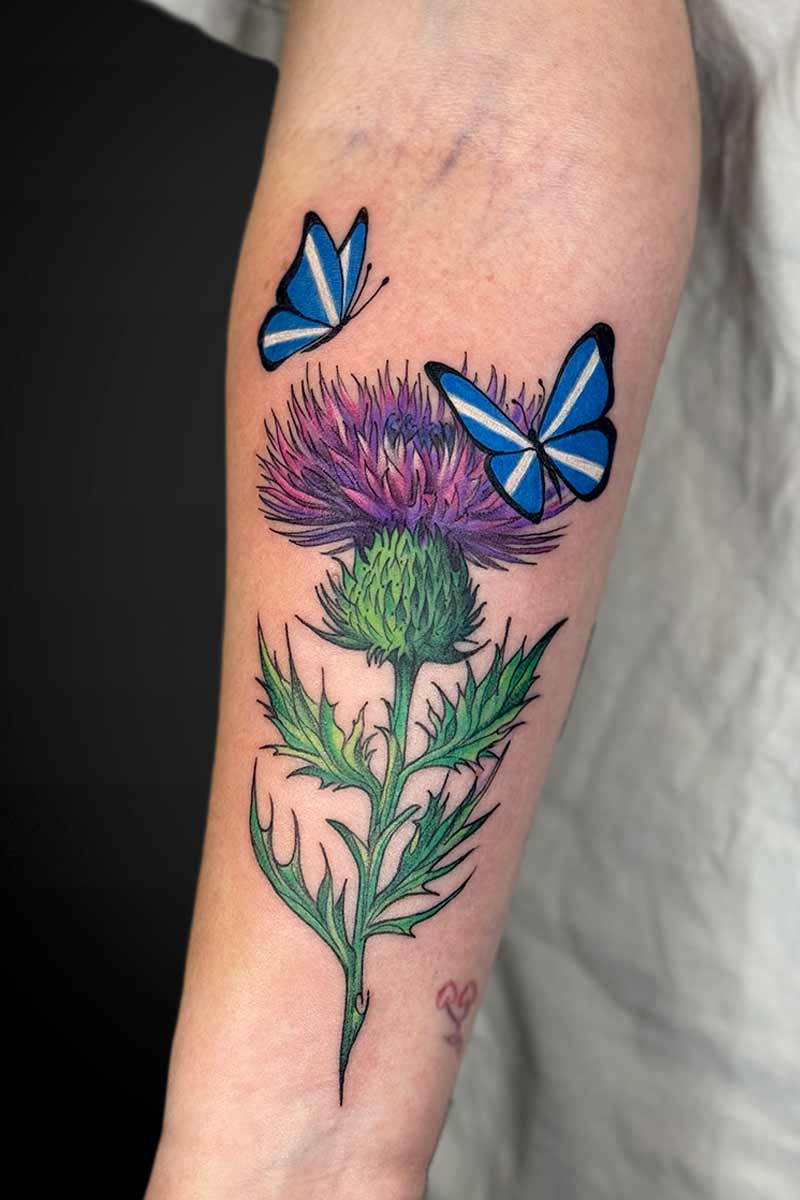 Legacy Tattoo| Colour, floral tattoo of a Scottish thistle with two butterflies with the Scottish flag