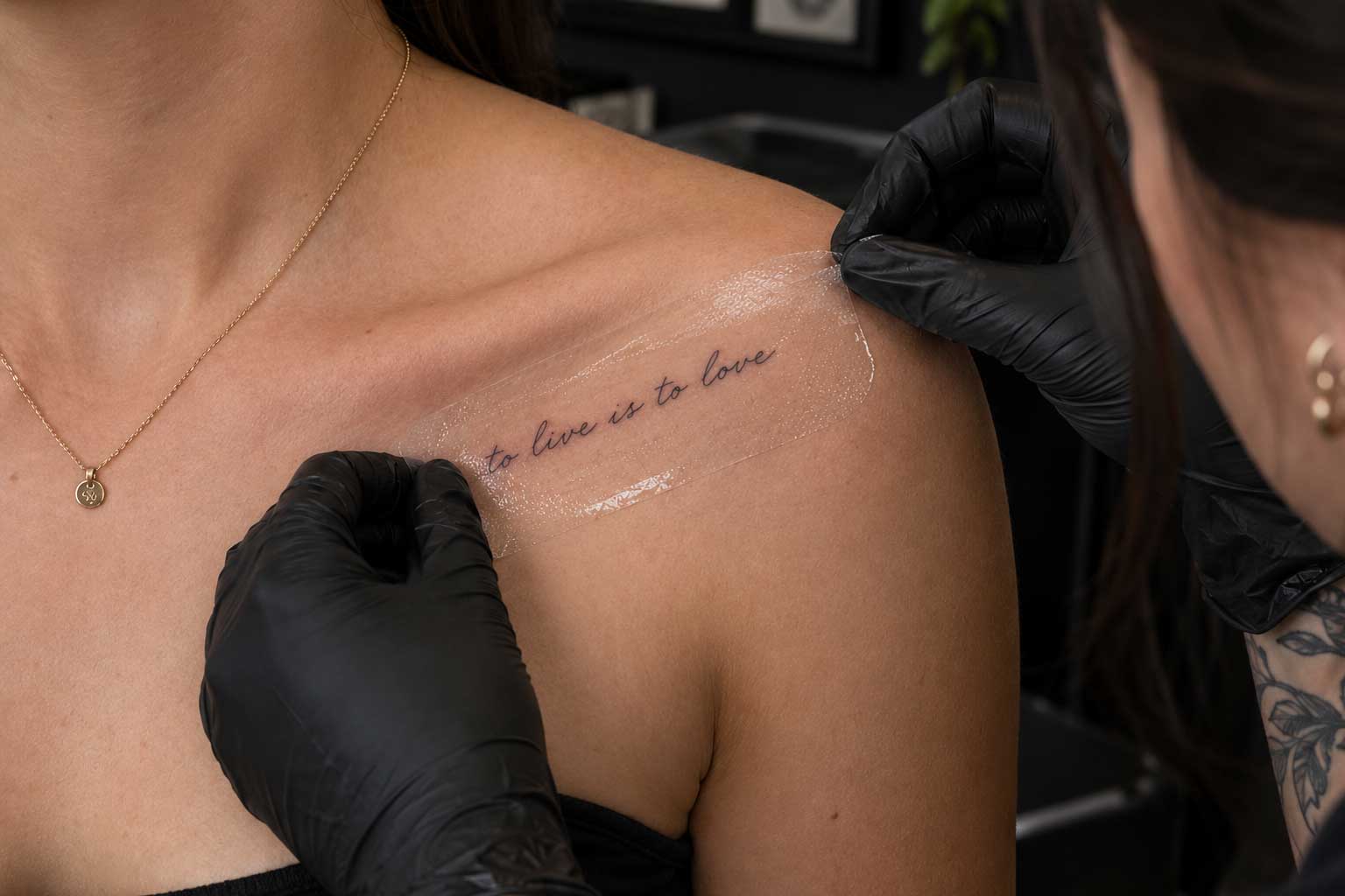 Tattoo artist in black gloves peeling a transfer stencil off a client’s collarbone at Legacy Tattoo in Calgary