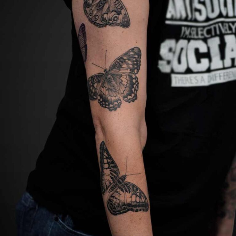 Black and white tattoos of detailed butterflies on a person's arm and shoulder.