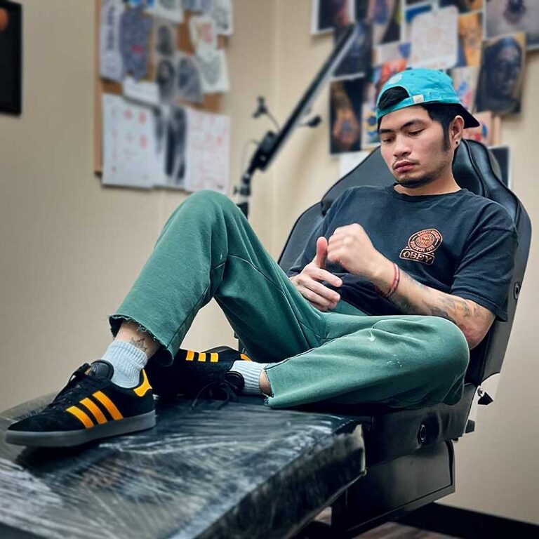 Man in teal cap and Obey shirt sitting in a tattoo chair.