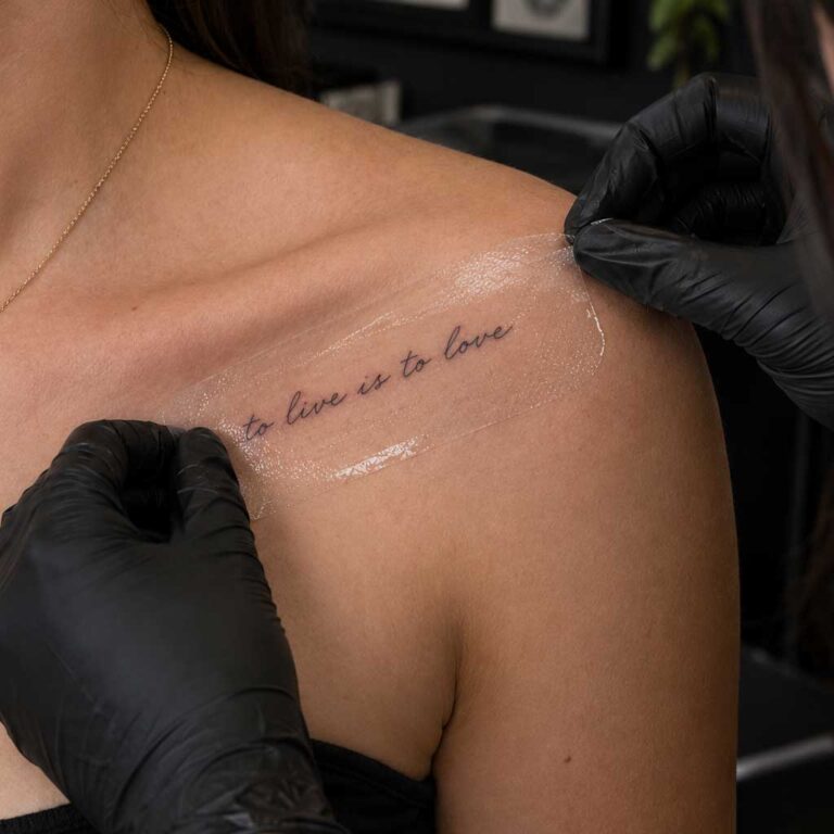 Tattoo artist in black gloves peeling a transfer stencil off a client’s collarbone at Legacy Tattoo in Calgary
